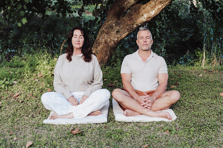 Two adults meditating outdoors under a tree