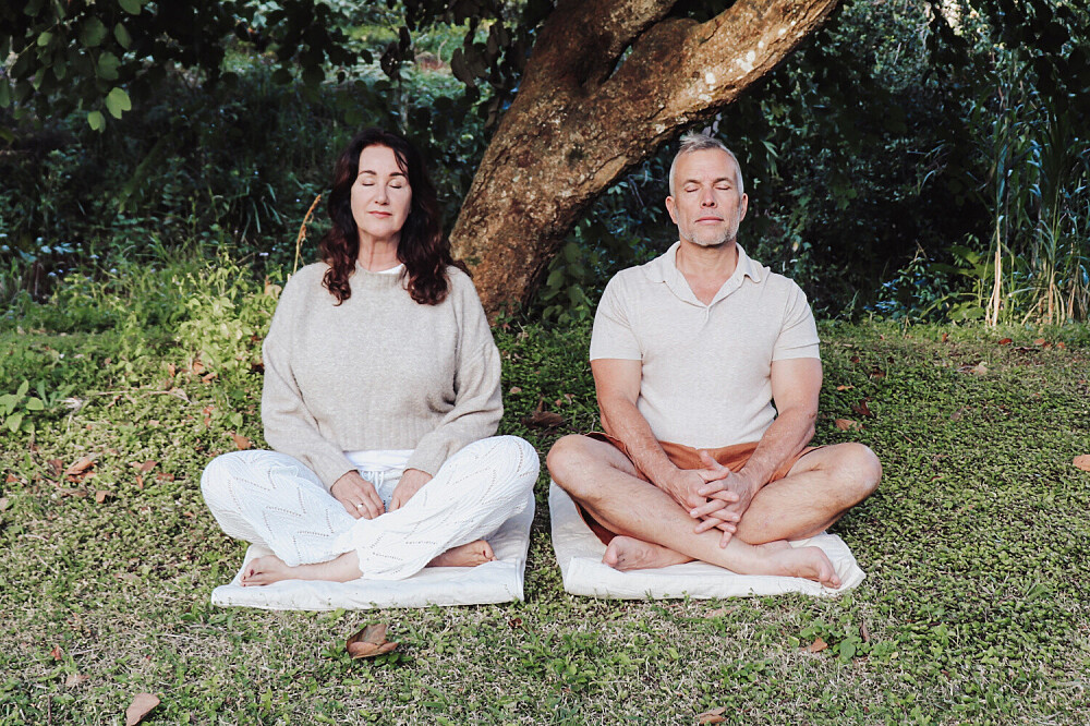 Two adults meditating outdoors under a tree
