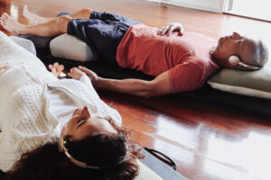 Two adults lying on cushions wearing headphones indoors