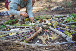 Person creating nature mandala with sticks and flowers