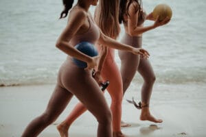 Three women walking on beach with exercise equipment
