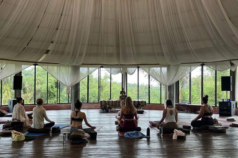 Group meditating in open-air pavilion with greenery views