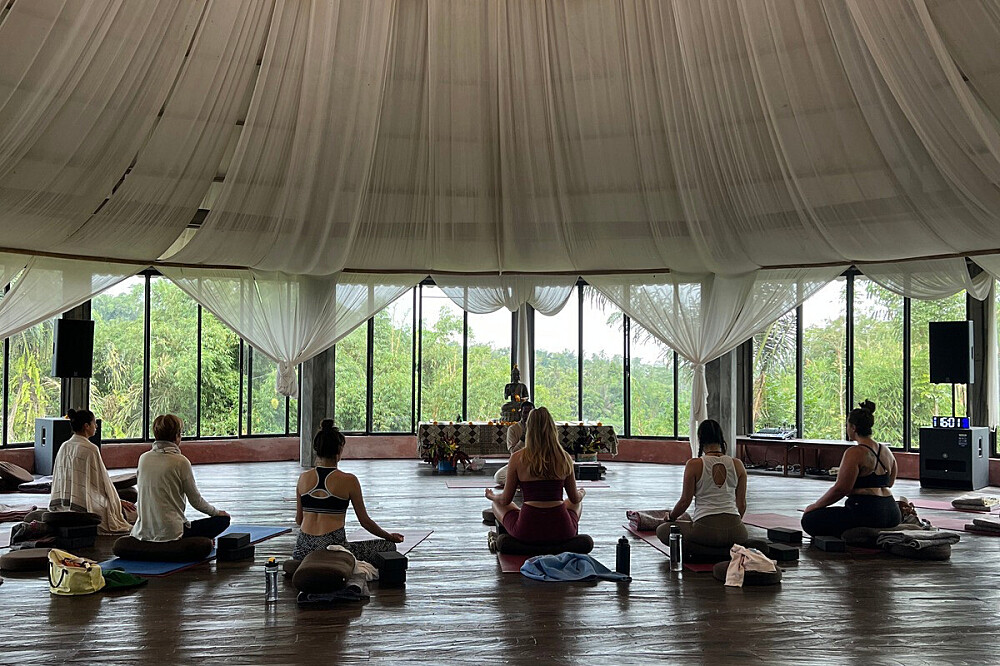 Group meditating in open-air pavilion with greenery views