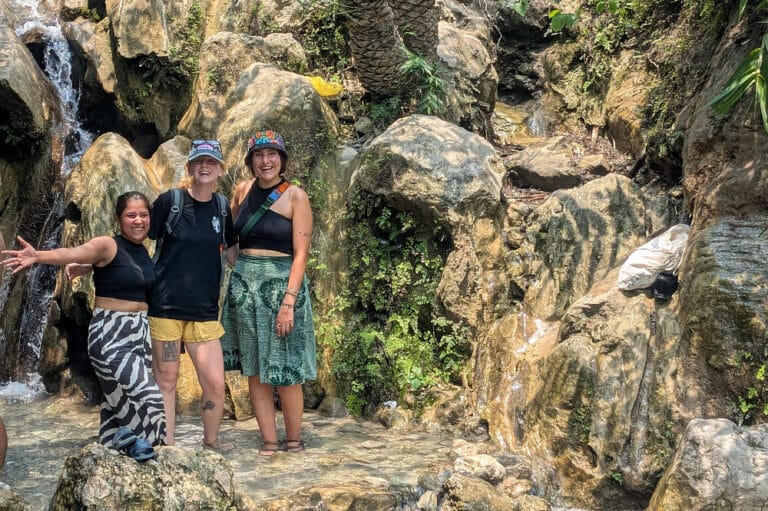 Three women standing by rocky waterfall stream