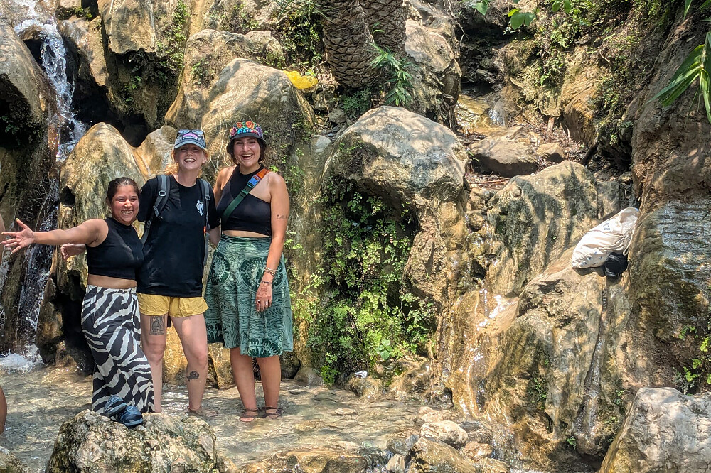 Three women standing by rocky waterfall stream