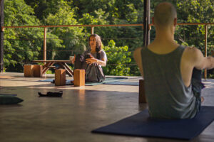 Outdoor yoga class on wooden deck surrounded by greenery