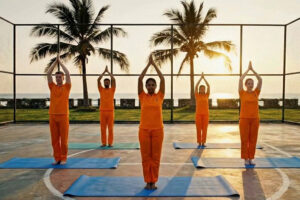Group practicing yoga outdoors at sunset by palm trees