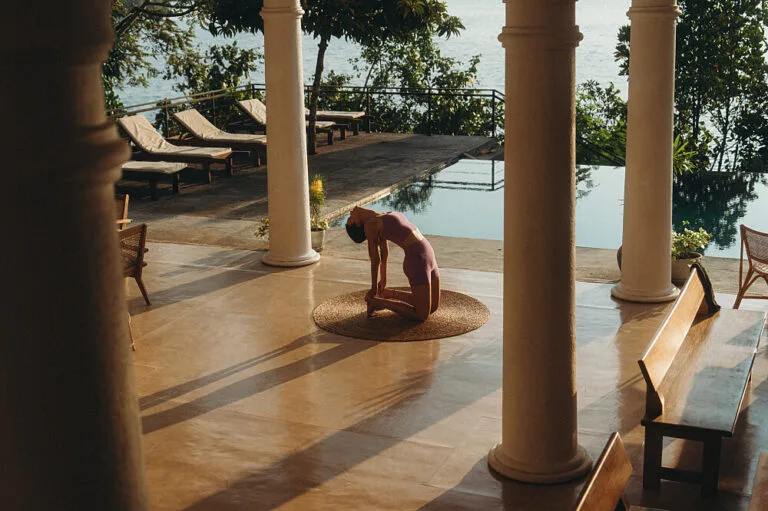 Woman practicing yoga on terrace by infinity pool