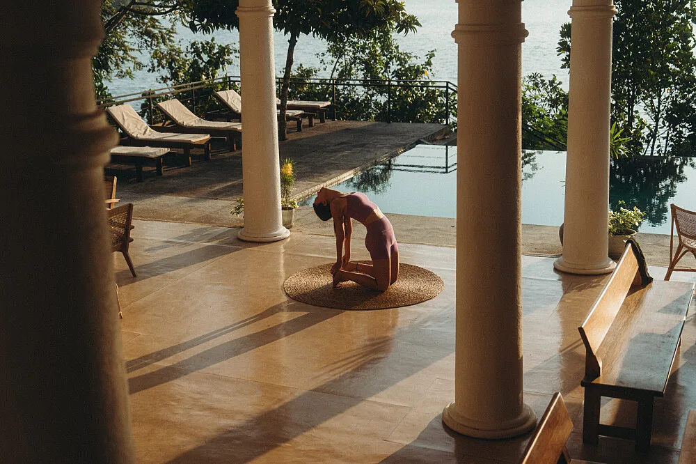 Woman practicing yoga on terrace by infinity pool