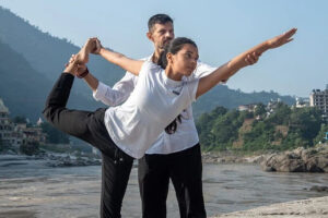 Couple practicing yoga by riverside at sunrise