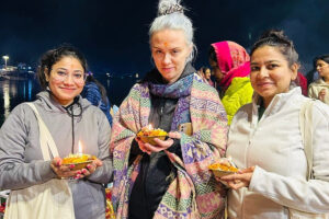 Three women holding lit diyas at night ceremony