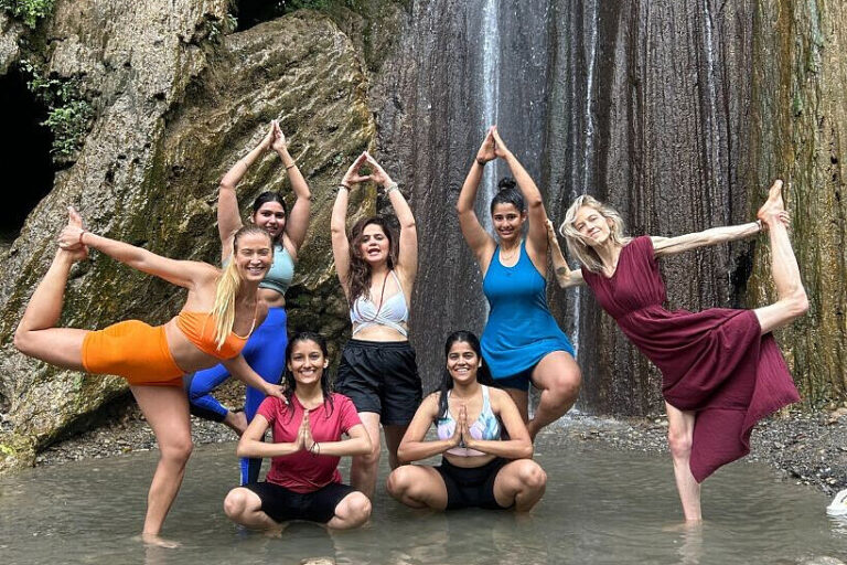 Women practicing yoga in waterfall pool