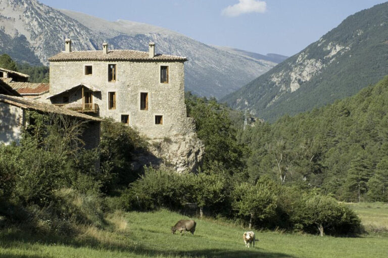 Stone house overlooking mountain valley with grazing cows