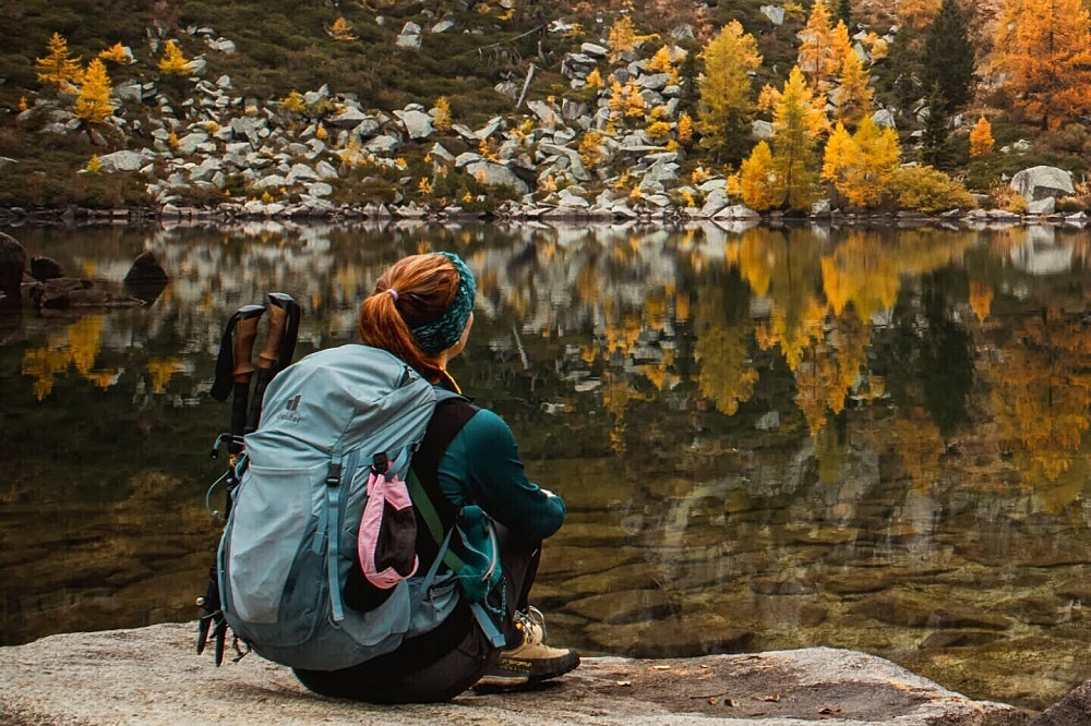 Hiker with backpack by reflective autumn lake