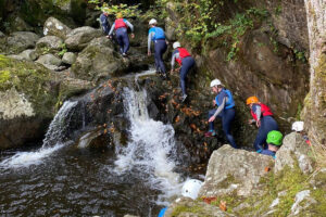 Group canyoning up rocky waterfall in forest