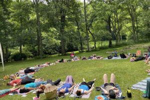 People lying on mats in wooded park clearing