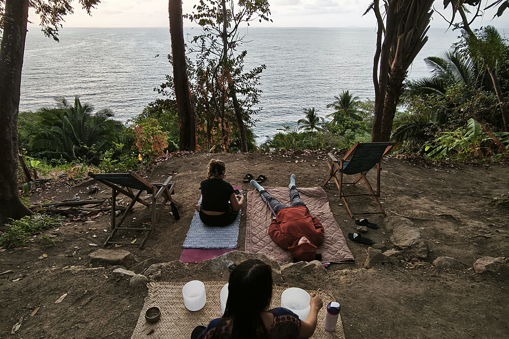 Three people relaxing on mats overlooking ocean