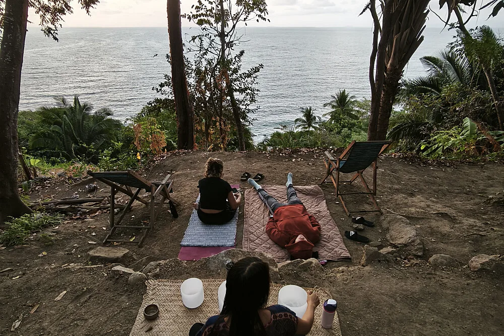 Three people relaxing on mats overlooking ocean