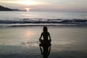 Silhouette meditating on beach at sunset