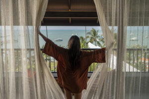 Woman opening curtains to ocean view balcony
