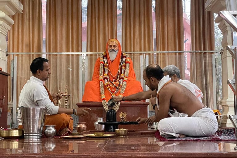 Priests performing Hindu ritual before seated guru statue