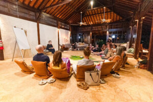 Group seated on cushions in open-air pavilion workshop