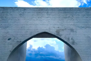 White stucco arch framing blue sky and clouds