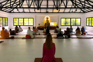 People meditating in bright hall with Buddha statue