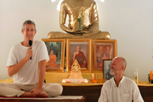 Man speaking before golden Buddha statue indoors
