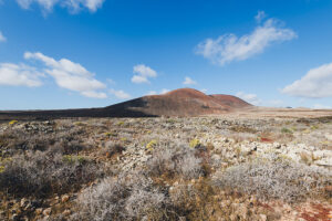 Volcanic hill in arid desert landscape under blue sky
